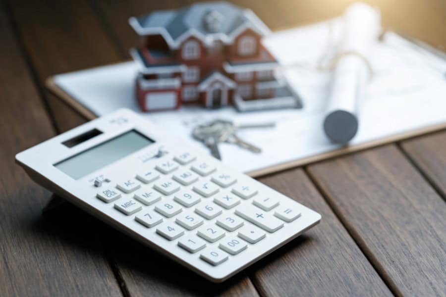 Berechnung des Immobilienwerts – Bauplan und Taschenrechner neben Hausmodell